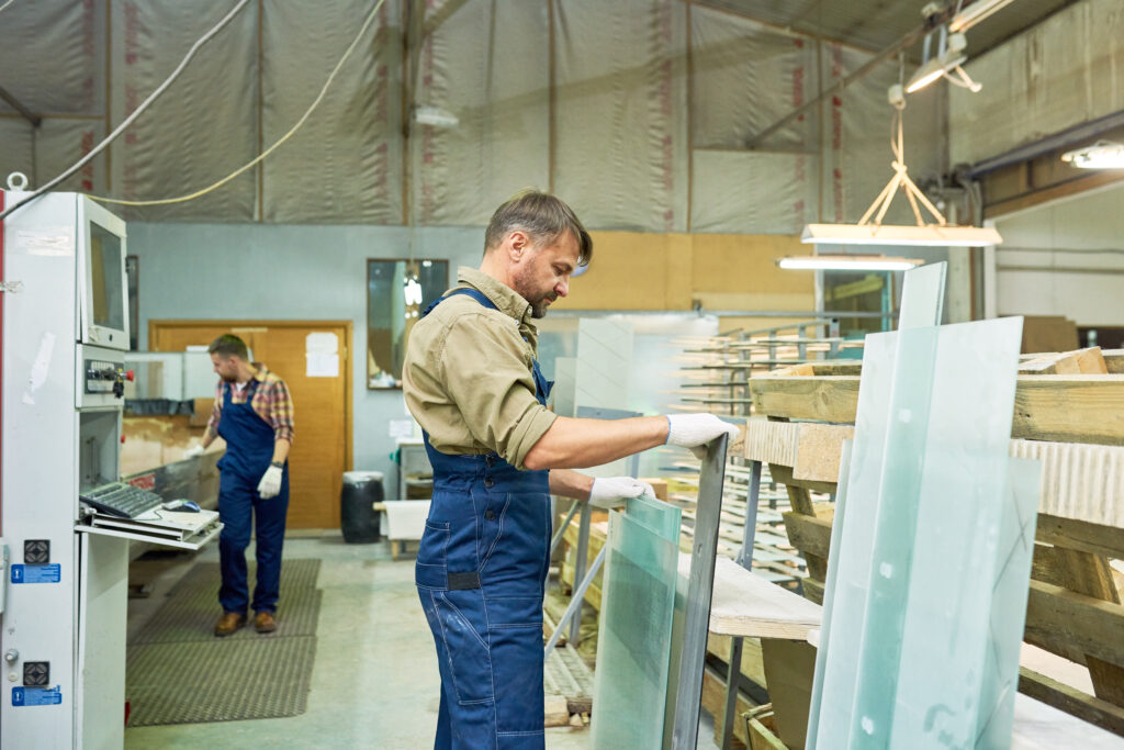 Busy workers in a modern furniture factory handling glass panels, showcasing craftsmanship and attention to detail in a professional setting.