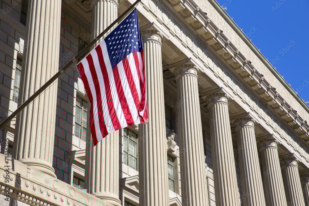 American flag waving in front of a historic government building with classical columns, symbolizing security and public service.